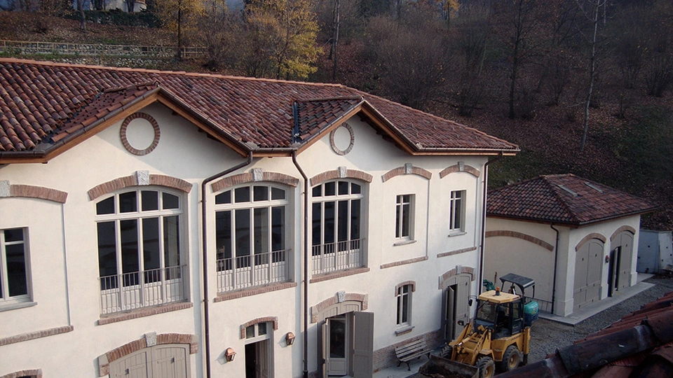 Edificio annesso alla villa con facciate restaurate, grandi finestre e mezzo da cantiere nel cortile.
