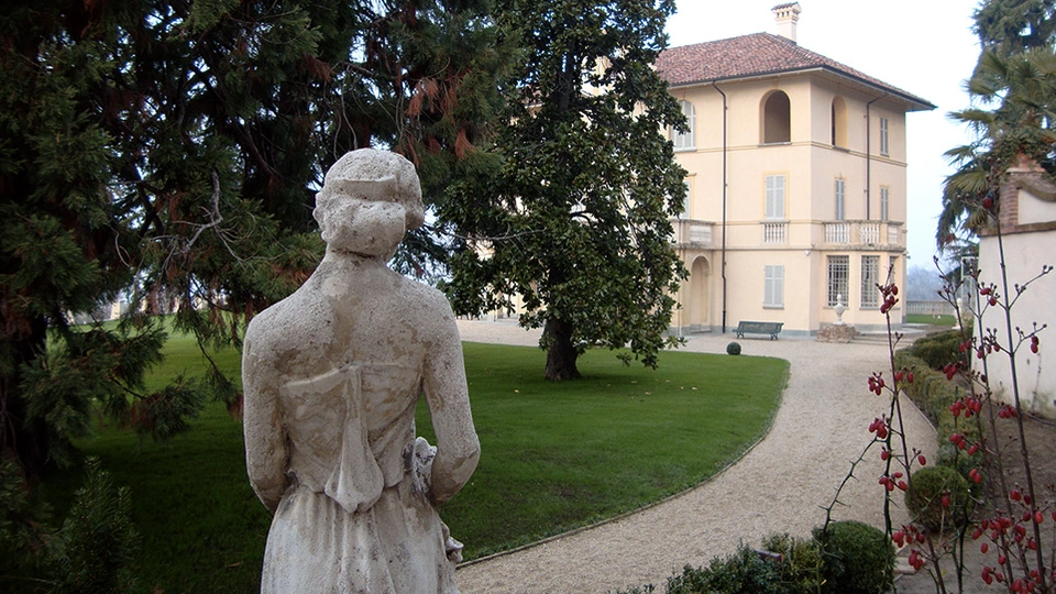 Statua in pietra vista di spalle lungo il percorso del giardino, con la villa sullo sfondo.